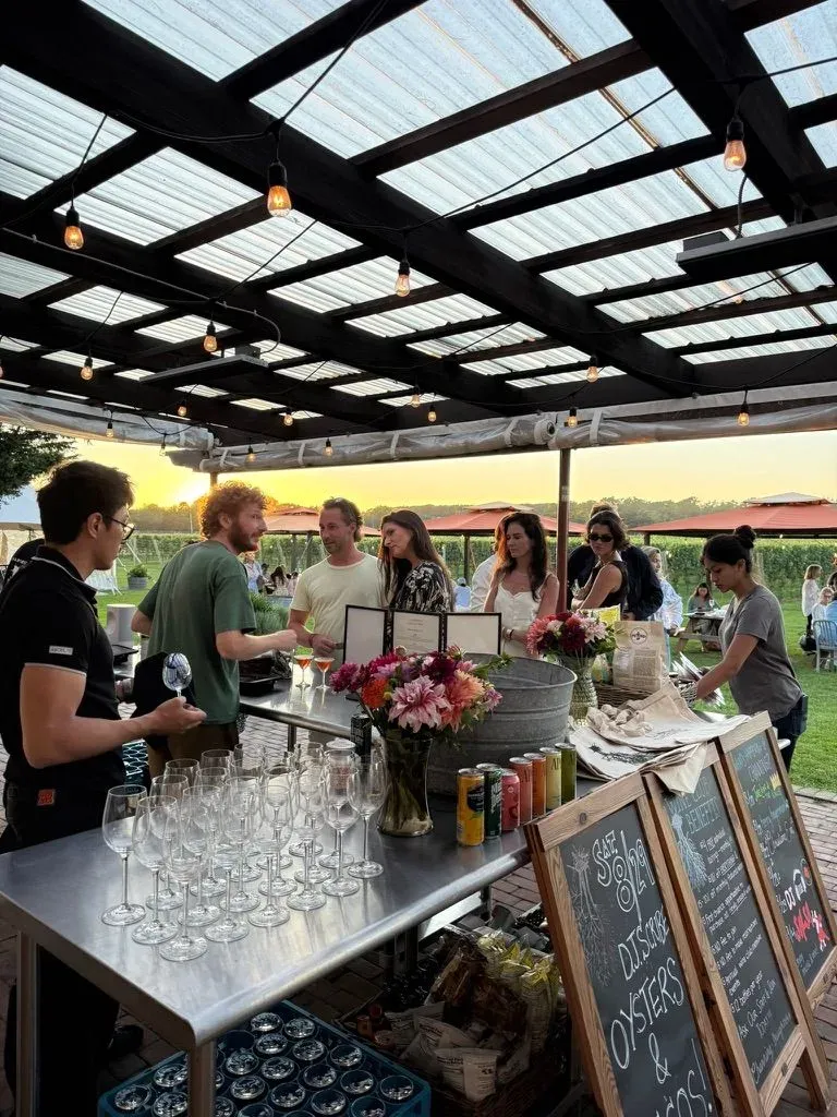 A group of people standing at an outdoor bar at sunset.