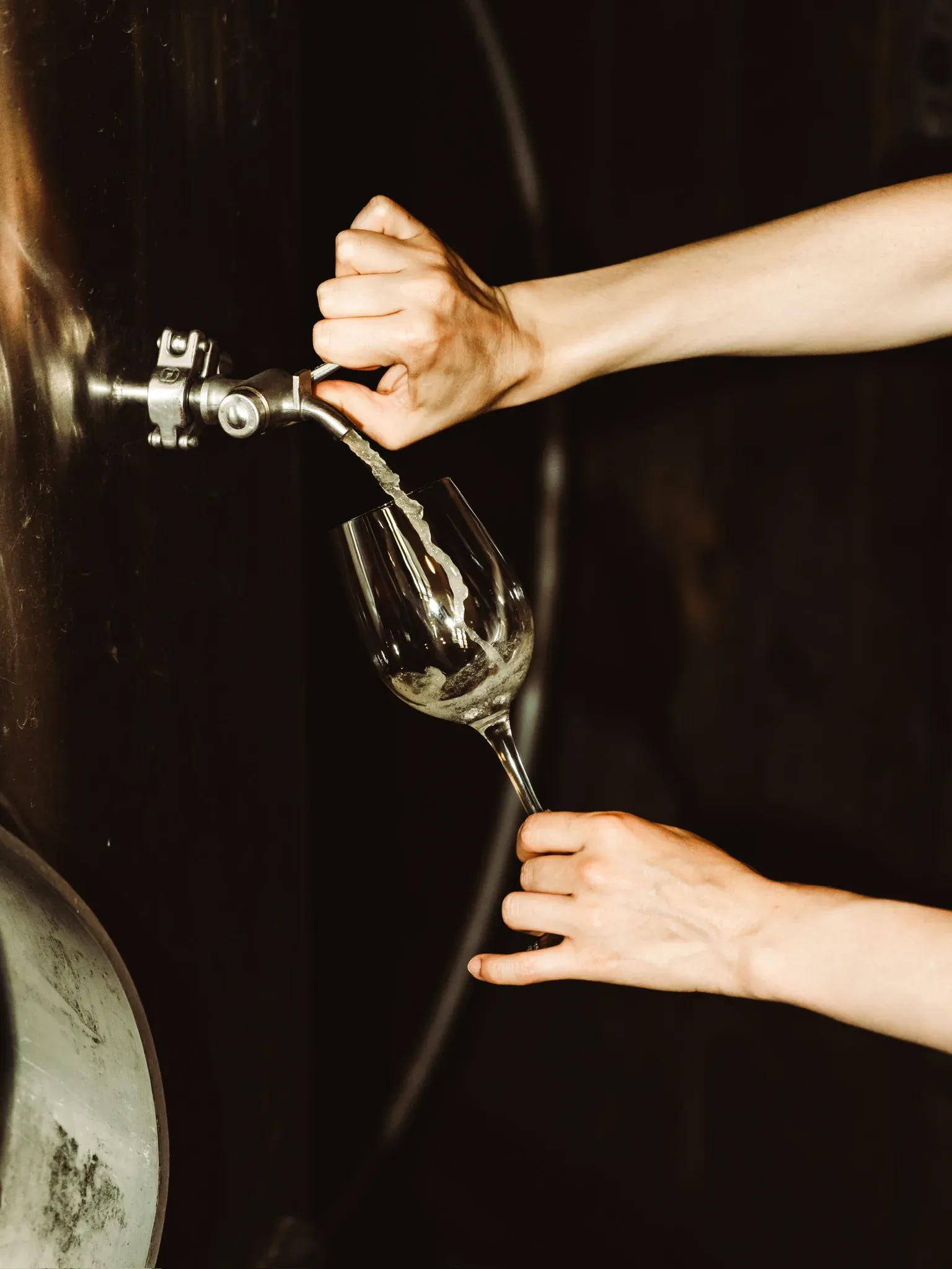 Two hands filling a wine glass from the tap of a tank