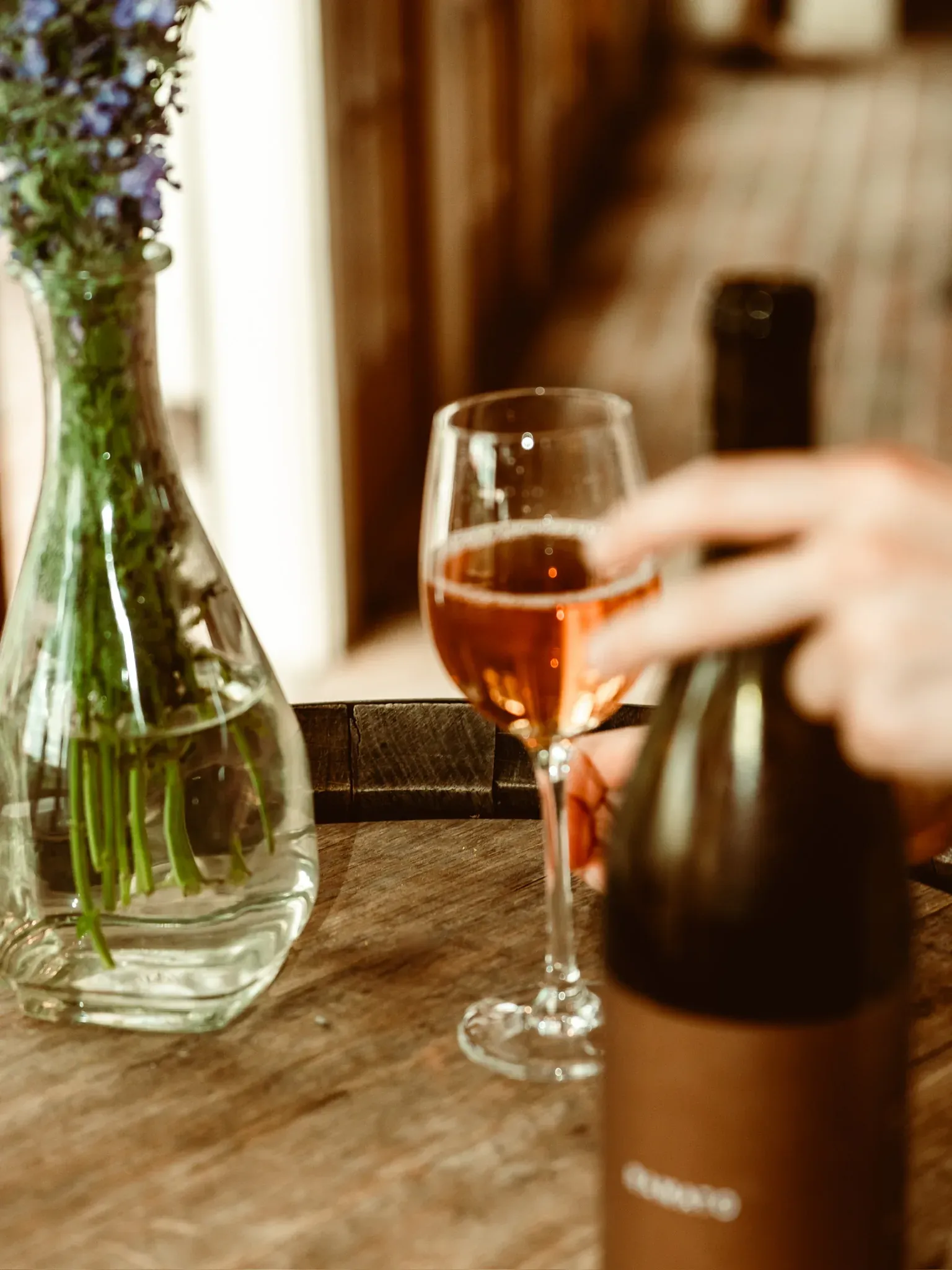 A glass of rosé held beside a bottle at the wooden bar