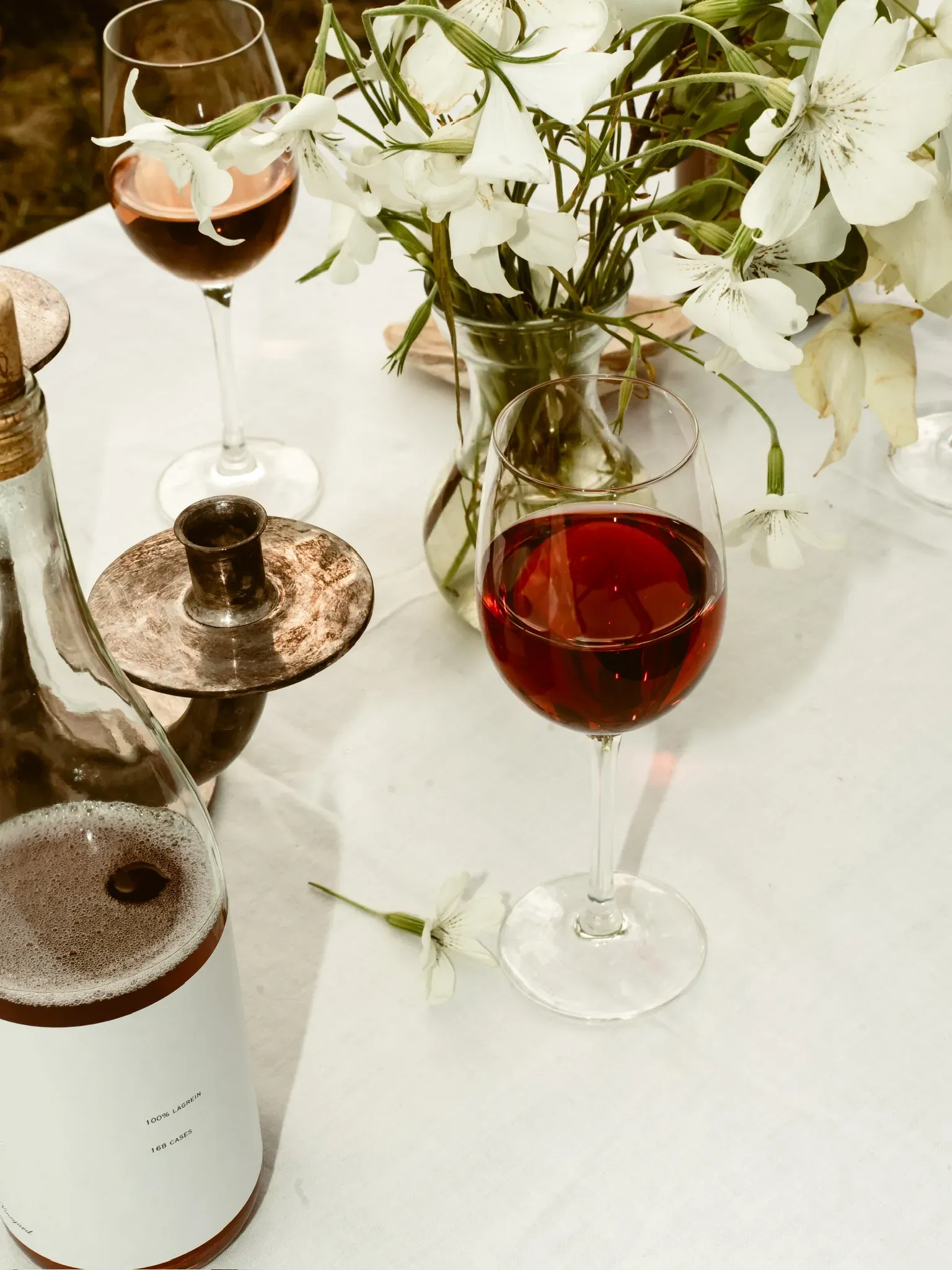 A glass of rosé beside a jug of white flowers on linen
