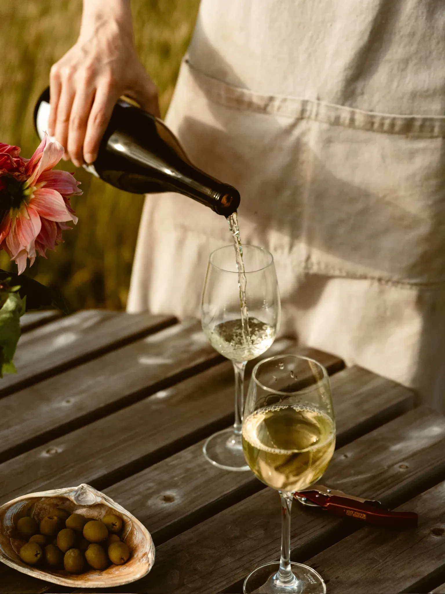 White wine poured at a picnic table, a dish of olives beside it