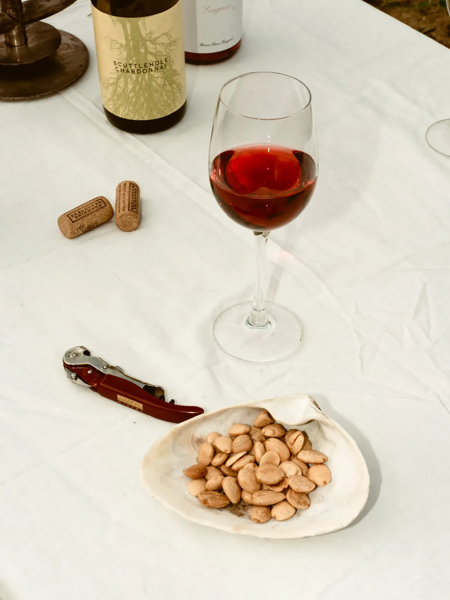 A glass of red wine, corks and a dish of almonds on a white tablecloth